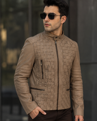 Man wearing a brown quilted jacket and sunglasses against a blurred background