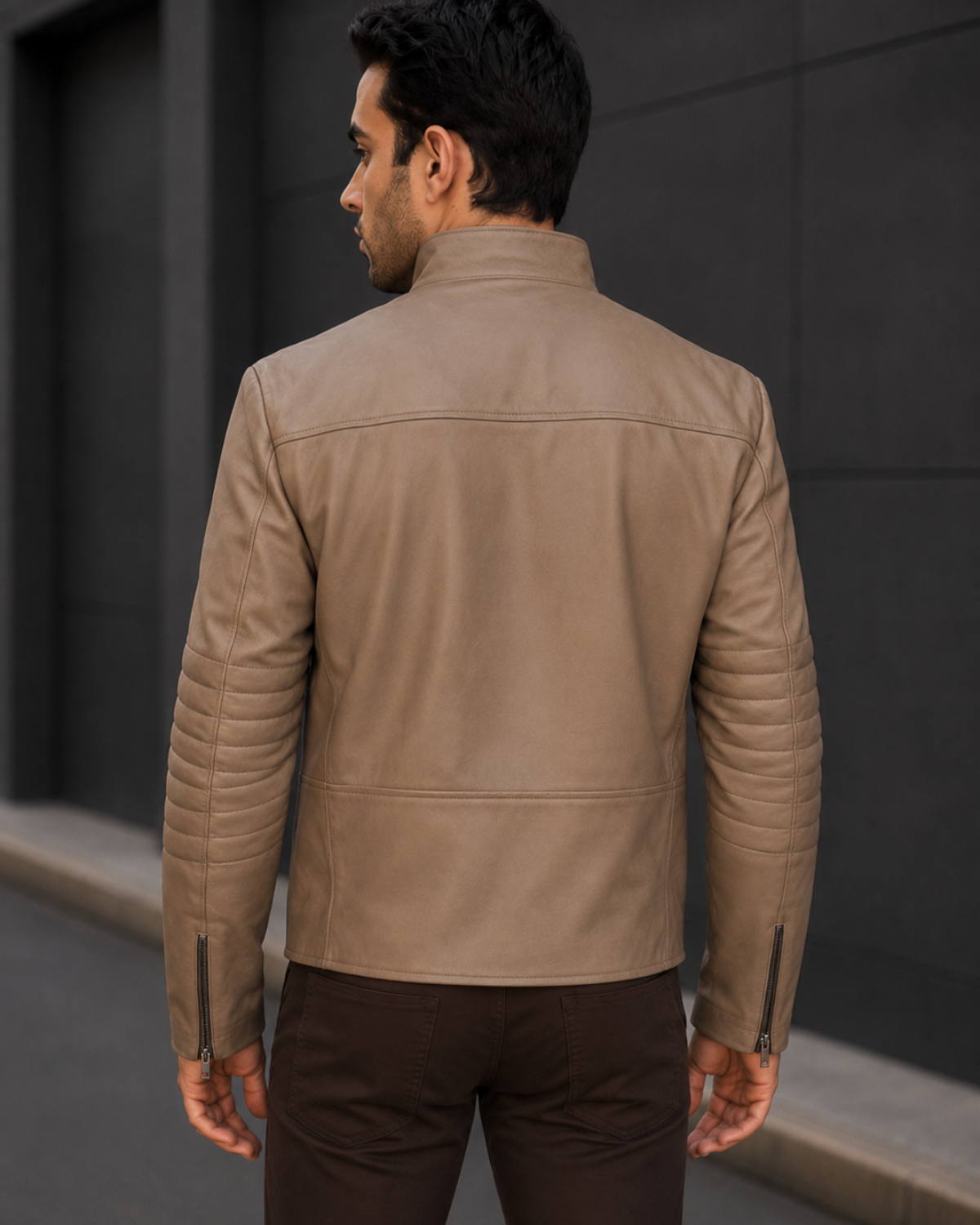 Man wearing a beige leather jacket standing against a dark wall.