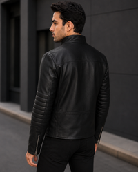 Man wearing a black leather jacket standing against a dark wall.