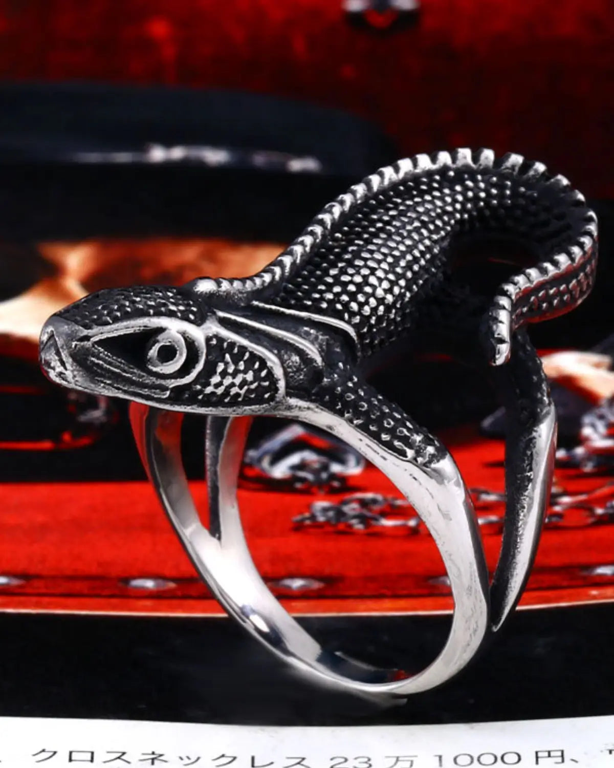 A silver-toned ring sculpted in the shape of a lizard or snake, shown close up against a dark red and black background.