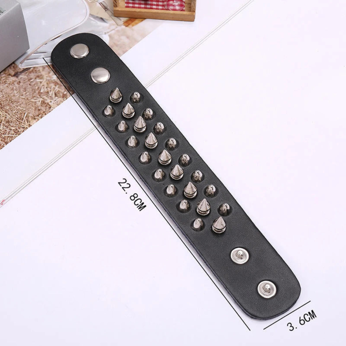 A black leather wristband or bracelet strap laid diagonally on a white surface, decorated with multiple silver metal spikes of varying sizes and three silver rivets. Black text on the image shows dimensions: 22.