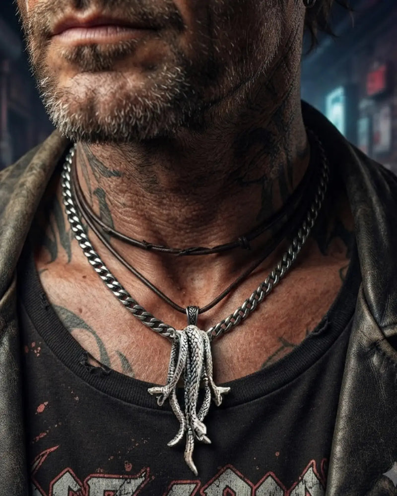 A close-up lifestyle shot of a man's neck and chest wearing multiple layered necklaces, including a silver snake pendant on a chain over a black t-shirt.