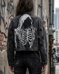 Person wearing a black denim jacket with a skeleton design on the back, standing against a graffiti-covered wall.
