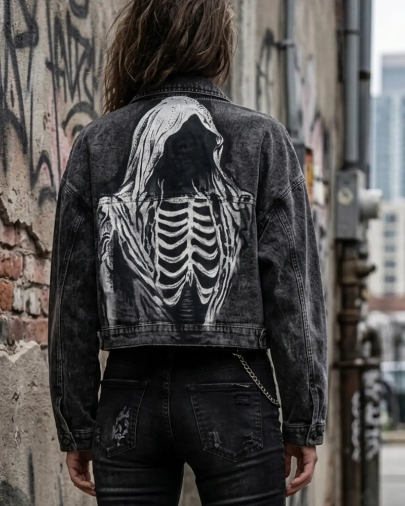 Person wearing a black denim jacket with a skeleton design on the back, standing against a graffiti-covered wall.