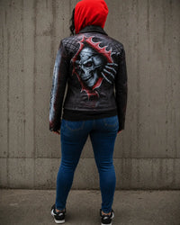 Person wearing a black leather jacket with a skull design against a gray wall. Vanna Women's Hand-Painted Punisher Skull Real Lamb Leather Motorcycle Jacket
