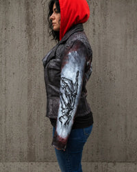 Person wearing a dark jacket with a red hood and a tattooed arm against a concrete wall. Vanna Women's Hand-Painted Punisher Skull Real Lamb Leather Motorcycle Jacket
