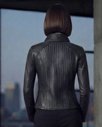 A woman viewed from behind wearing a fitted black leather jacket with a textured, scale-like pattern across the back and shoulders, set against a blurred cityscape background.