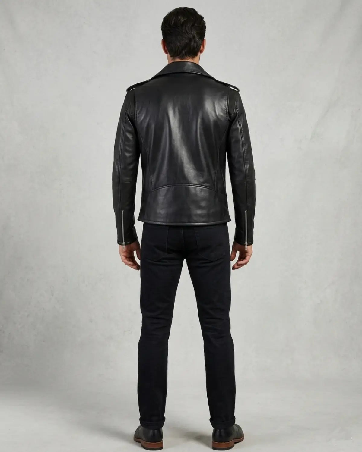 A man viewed from the back wearing a black leather biker jacket, black pants.