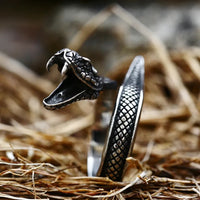 A silver-colored stainless steel ring with a vintage snake design, displayed on a straw background.